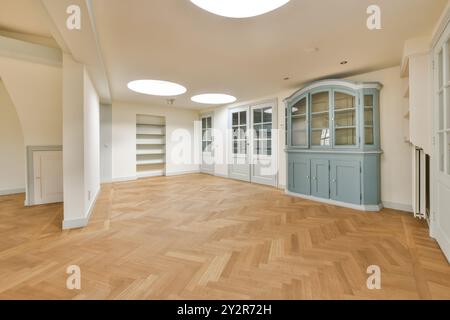 Ein geräumiges, unmöbliertes Zimmer mit poliertem Fischgrätparkett, weißen Wänden mit glatter geschwungener Decke und grauen Einbauschränken. Stockfoto