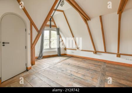 Leerer Raum im Dachgeschoss mit freiliegenden Holzbalken, Hartholzfußboden und einem Fenster, das natürliches Licht einlässt. Stockfoto