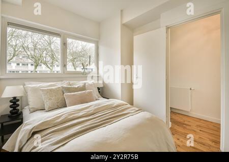 Ein ruhiges Schlafzimmer mit einem komfortablen Bett mit weichen Kissen, großen Fenstern für Tageslicht und einer einfachen, eleganten Einrichtung. Stockfoto