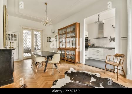 Ein elegantes Esszimmer mit klassischem Tischset, Kronleuchter und Stall, mit offenem Eingang zu einer modernen Küche. Stockfoto