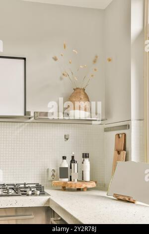 Eine elegante, moderne Küche mit einer strukturierten Vase mit getrockneten Pflanzen auf einem Regal und verschiedenen Flaschen auf einem Holztablett auf der Arbeitsplatte. Stockfoto