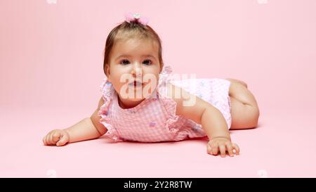 Kleine süße kleine Prinzessin, die die Welt erforscht, gekleidet in rosa Strampelanzug mit passender Schleife vor weichem rosa Hintergrund. Stockfoto