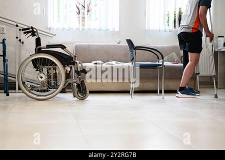 Ein Mann mit Krücken geht in eine Reha-Einrichtung neben einem Rollstuhl. Das Setting hebt Mobilitätshilfen und Rehabilitationstherapie in einer modernen Heilung hervor Stockfoto