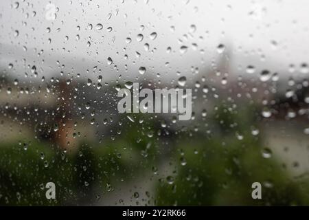 Die Regentropfen an einem Fenster mit verschwommenem Blick auf Gebäude und Bäume im Hintergrund Stockfoto