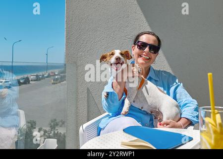 Porträt der lächelnden Frau und ihres Jack Russell Terrier Haustieres auf dem Balkon des Hotels. Schöne europäische Frau mittleren Alters und ihr Hund verbringen Zeit miteinander Stockfoto