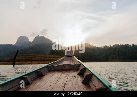 Das Licht des frühen Morgenlichts strahlt ein warmes Leuchten über den ruhigen See und hebt die Berge in der Ferne hervor, während ein hölzernes Boot sanft auf dem Wasser schwimmt. Stockfoto