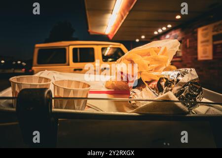Eine Nahaufnahme einer Fast-Food-Mahlzeit auf einem Tablett mit einem Auto im Hintergrund in einem Drive-in-Diner am Abend. Stockfoto