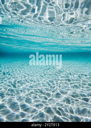 Unterwasserblick auf klares türkisfarbenes Wasser mit Sonnenlicht, das Wellen auf dem Sandboden erzeugt. Stockfoto