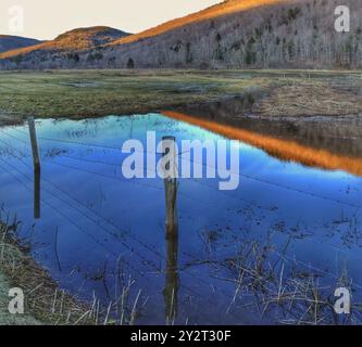 Ein überflutetes Feld im Frühling in Vermont mit Reflexionen auf das stille Wasser und einem alten Zaun mit Stacheldraht Stockfoto