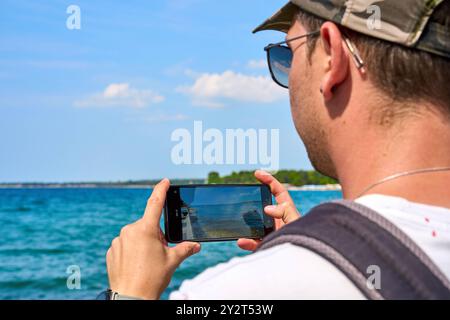 Porec, Istrien, Kroatien - 27. August 2024: Ein Tourist fotografiert das Meer in Porec, Kroatien, mit seinem Smartphone und hält so einen Moment seines Sommerurlaubs fest Stockfoto
