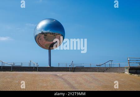 Ein großer, reflektierender Glitzerkugel an einer Strandpromenade. Die Kugel ist an einem einzigen zentralen Pol montiert und reflektiert die umgebende Umgebung Stockfoto