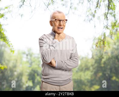 Ein älterer Mann mit Halsschmerzen, der draußen in einem Park steht Stockfoto