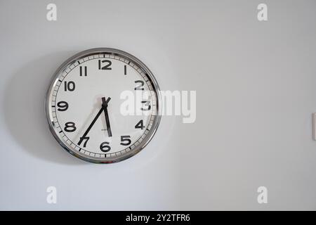 Analoge Uhr an einer minimalistischen Wand mit klaren Zahlen und Zeigern, die die Zeit anzeigen. Einfach und funktional. Stockfoto