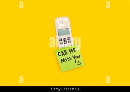 Ein klebriges Papier mit dem Phrase "Call Me Miss You" auf einem Telefon auf gelbem Hintergrund Stockfoto