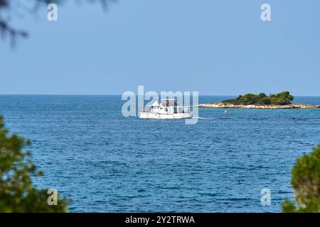 Porec, Istrien, Kroatien - 26. August 2024: Ein Boot kreuzt vor der Küste von Porec, Kroatien, und bietet eine ruhige Aussicht auf das kristallklare Meer und eine kleine Insel *** ein Boot kreuzt vor der Küste von Porec, Kroatien, und bietet eine ruhige Aussicht auf das kristallklare Meer und eine kleine Insel Stockfoto