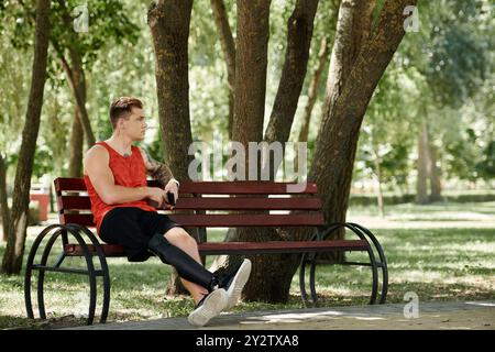 Ein junger Mann mit Tattoos sitzt auf einer Bank im grünen Park draußen Stockfoto