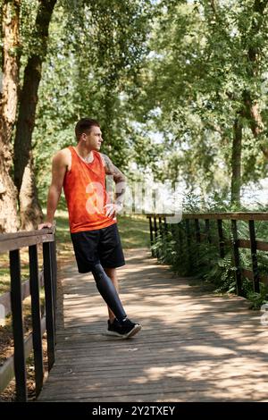 Ein junger Mann mit Tätowierungen und Beinprothesen steht stolz auf der Brücke, umgeben von Parkgrün. Stockfoto