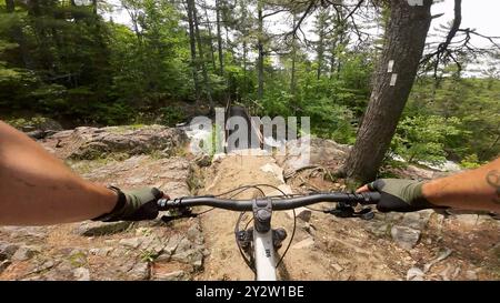 Weitwinkelansicht eines Mountainbikers, der sich einer Stahlbrücke über einen Wasserfall an einem felsigen Hang in den Hiawatha Highlands nähert Stockfoto