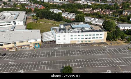 Blick aus der Vogelperspektive auf ein modernes Gebäude mit Solarpaneelen und einen angrenzenden leeren Parkplatz in einem Vorstadtbereich. Stockfoto