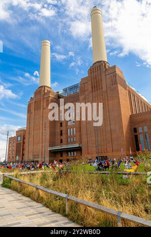 Leute sitzen in Liegestühlen auf dem Rasen vor dem Battersea Power Station, heute ein wichtiges Freizeit- und Einzelhandelsziel, Nine Elms, London Stockfoto