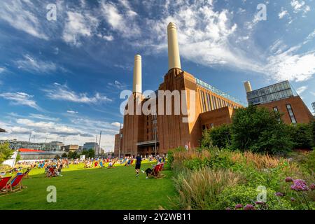 Leute sitzen in Liegestühlen auf dem Rasen vor dem Battersea Power Station, heute ein großes Freizeit- und Einzelhandelsziel, Nine Elms, London Stockfoto