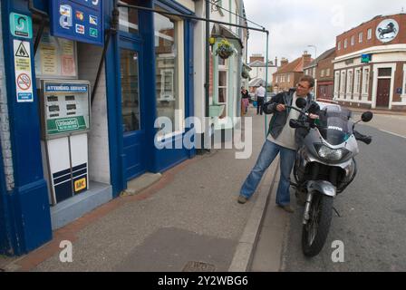 Altmodische Benzinpumpe mit Selbstbedienung, Schlauch auf der anderen Straßenseite. Ein Mann, der sein Motorrad auffüllt. Wainfleet Allerheiligen. Lincolnshire, England 2008 2000er Jahre, Großbritannien HOMER SYKES Stockfoto