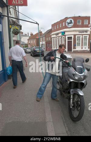 Altmodische Benzinpumpe mit Selbstbedienung, Schlauch auf der anderen Straßenseite. Ein Mann, der sein Motorrad auffüllt. Wainfleet Allerheiligen. Lincolnshire, England 2008 2000er Jahre, Großbritannien HOMER SYKES Stockfoto