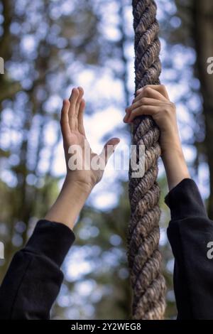 Eine Nahaufnahme der Hände, die ein dickes Seil mit einem verschwommenen Waldhintergrund greifen Stockfoto
