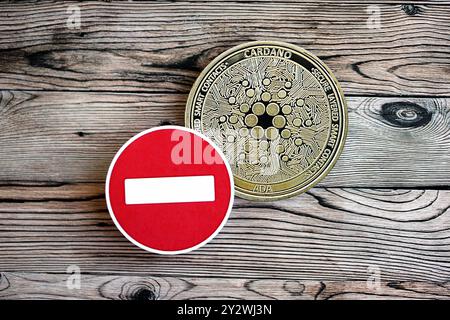 KIEW, UKRAINE - 17. AUGUST 2024 Cardano ADA Münze und rotes Papier Stoppschild auf hölzernem Hintergrund Nahaufnahme Stockfoto