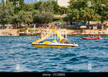 Porec, Istrien, Kroatien - 27. August 2024: Die Familie genießt eine Fahrt in einem Tretboot mit einer Rutsche vor der Küste von Porec, Kroatien. Sommer, Spaß und Entspannung am Meer *** Familie genießt eine Fahrt im Tretboot mit Rutsche vor der Küste von Porec, Kroatien. Sommer, Spaß und Entspannung am Meer Stockfoto