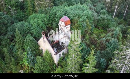 Ein Blick aus der Vogelperspektive auf eine alte Holzhütte in der Nähe eines neuen Damms und eines Flusses und eines Kraftwerks in einem grünen Wald Stockfoto