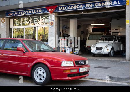 Ein Mechaniker aus einer Werkstatt in Barcelona. Im Inneren befindet sich ein alter, klassischer weißer Citroen 2cv und draußen ein schönes rotes Audi Coupé Stockfoto