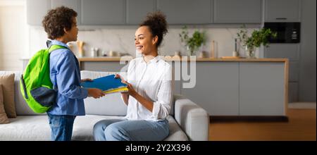 Eine Mutter verwickelt sich mit ihrem Sohn, indem sie Bücher in einer gemütlichen Küche teilt Stockfoto