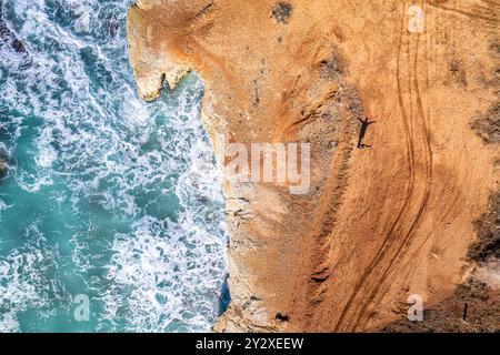 Aus der Vogelperspektive einer Person, die auf einer Klippe neben dem Meer steht, mit Wellen, die gegen die Felsen darunter krachen. Stockfoto