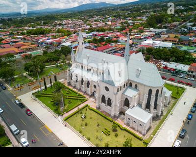Blick aus der Vogelperspektive auf die Basilika der Unbefleckten Empfängnis in Heredia, Costa Rica, umgeben von üppigem Grün und farbenfrohen Gebäuden Stockfoto