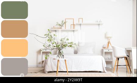 Vase mit blühenden Zweigen auf dem Tisch neben dem gemütlichen Bett im weißen Schlafzimmer. Verschiedene Farbmuster Stockfoto
