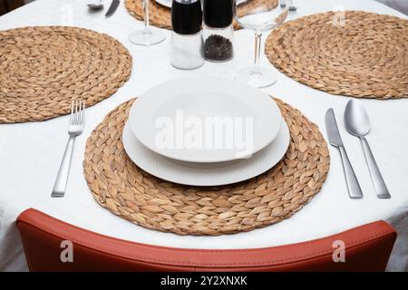 Geschmackvoll angeordnete weiße Teller auf gewebten Tischsets mit Besteck, Gläsern und Shakern auf einem sauberen romantischen Tisch Stockfoto