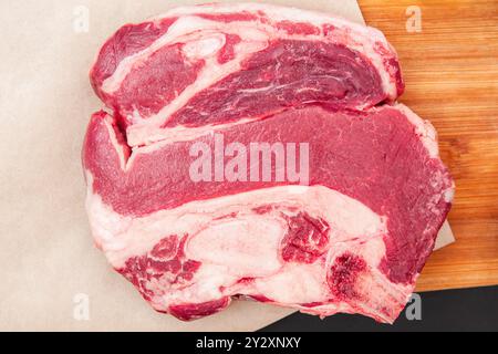 Dickes rohes Rindersteak auf hölzernem Schneidebrett mit Kräutern, Steak zum Würzen und Kochen Stockfoto