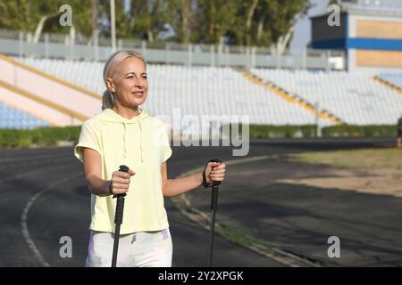 Schöne reife glückliche Frau, die mit Gehstöcken im Stadion trainiert Stockfoto