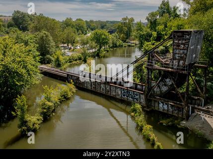 Ein malerischer Blick auf eine rostfreie Eisenbahnbrücke über einen Fluss, umgeben von üppigem Grün an einem sonnigen Tag. Stockfoto
