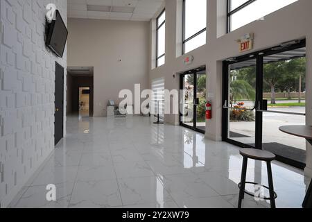 Eine leere, moderne Lobby mit großen Fenstern, weißem Marmorfußboden und minimalistischer Einrichtung mit wandmontiertem Fernseher und Ausgangstüren. Stockfoto