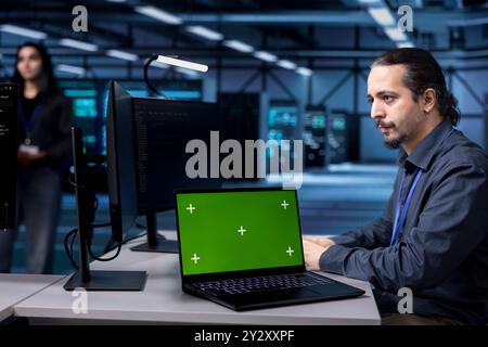 Techniker verwenden einen Green-Screen-Laptop zur Wartung des Server-Hubs und verlängern so die Lebensdauer der Geräte. Mitarbeiter überwachen Mainframes im Rechenzentrum mit Modell-Notebook auf Überhitzungsprobleme Stockfoto