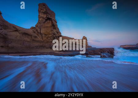 Eine atemberaubende Küstenlandschaft mit Felsformationen und Wellen, die bei Sonnenuntergang am Ufer abstürzen. Stockfoto