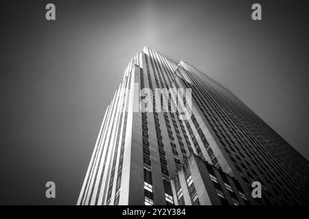 Schwarzweiß-Foto eines hohen Wolkenkratzers mit einer aufwärts gerichteten Perspektive, das seine architektonischen Details vor einem klaren Himmel zeigt. Stockfoto
