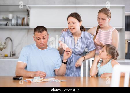 Ehepartner diskutieren unangenehme finanzielle Probleme in der Küche, irritierte Ehefrau nimmt Geld vom Ehemann Stockfoto