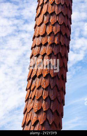 Eine Nahaufnahme eines strukturierten Holzpfahls mit einem einzigartigen schuppenartigen Muster vor einem blauen Himmel mit verstreuten Wolken. Stockfoto