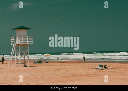 Leerer Strand mit weißer Rettungswache am Horizont am blauen mittelmeer. Holzhütte am morgendlichen Sandstrand. Holzweg führt zum Wasser. Stockfoto