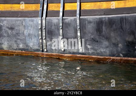 Nahaufnahme eines Bootsrumpf mit Metallbefestigungen und Holzakzenten, teilweise in Wasser getaucht. Stockfoto