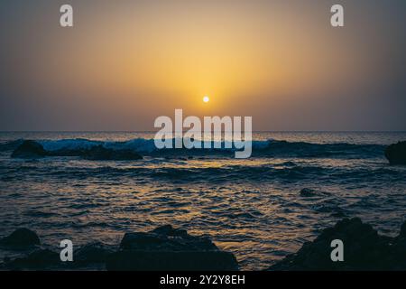 Ein ruhiger Sonnenuntergang über einem ruhigen Meer mit sanften Wellen in Tanger, Marokko Stockfoto