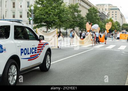 Washington DC, USA - 19.08.2024: Ein Polizeiauto parkt am Straßenrand. Eine Gruppe von Leuten marschiert auf der Straße Stockfoto